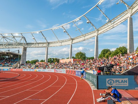 Innenansicht des Stadions bei einer Leichtathletikveranstaltung mit roter Laufbahn, Fotograf im Vordergrund und vollen Zuschauerrängen.