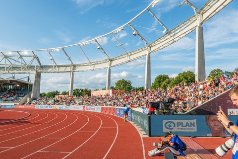 Innenansicht des Stadions bei einer Leichtathletikveranstaltung mit roter Laufbahn, Fotograf im Vordergrund und vollen Zuschauerrängen.