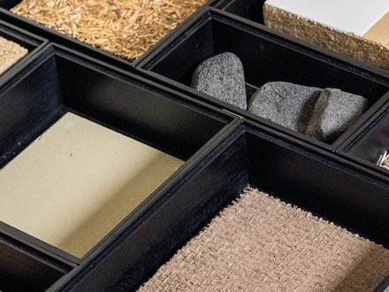 ahaufnahme einer Musterbox: mehrere Fächer mit verschiedenen Bau‑ und Dämmstoffen, überwiegend Naturmaterialien.