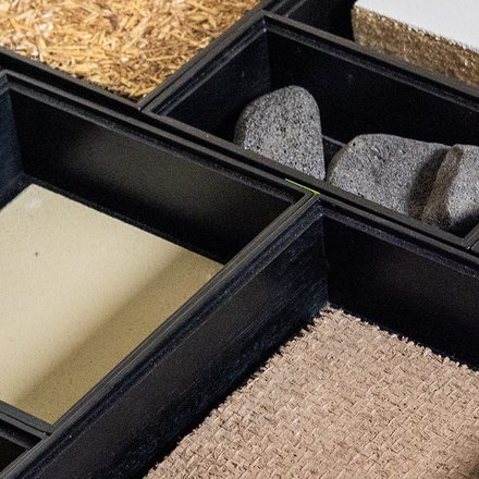 ahaufnahme einer Musterbox: mehrere Fächer mit verschiedenen Bau‑ und Dämmstoffen, überwiegend Naturmaterialien.