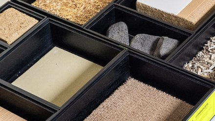 ahaufnahme einer Musterbox: mehrere Fächer mit verschiedenen Bau‑ und Dämmstoffen, überwiegend Naturmaterialien.