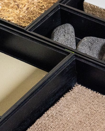ahaufnahme einer Musterbox: mehrere Fächer mit verschiedenen Bau‑ und Dämmstoffen, überwiegend Naturmaterialien.