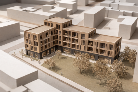 Foto eines Architekturmodells: L‑förmiges Holzgebäude mit verglastem Erdgeschoss und grünem Hof.