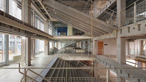 Mehrstöckiger Innenraum eines Rohbaus mit Treppen und weißen Gittergeländer. 
