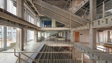 Mehrstöckiger Innenraum eines Rohbaus mit Treppen und weißen Gittergeländer. 