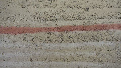 Stampflehm-Detail mit waagerechten Schichten; mittig eine rötliche Ader im beigen Erdmaterial.