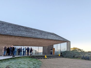 Besuchergruppe vor modernem Gebäude mit Reetdach bei einer Führung.