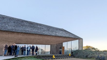 Besuchergruppe vor modernem Gebäude mit Reetdach bei einer Führung.