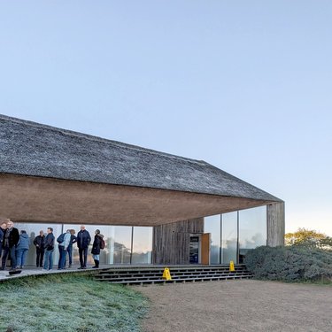 Besuchergruppe vor modernem Gebäude mit Reetdach bei einer Führung.