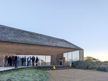 Besuchergruppe vor modernem Gebäude mit Reetdach bei einer Führung.