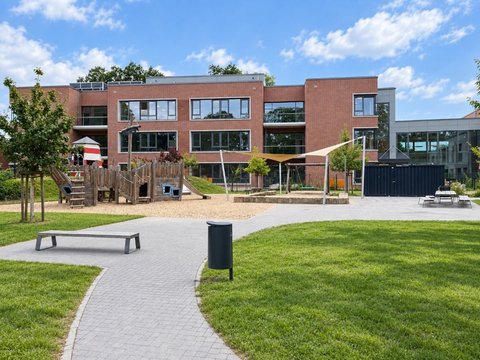 Moderner Backsteinbau einer Grundschule mit Spielplatz, Rasenfläche und gepflastertem Weg im Vordergrund