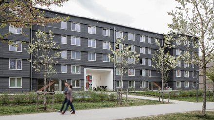 Ein grauen Wohnhaus mit grünen jungen Bäumen