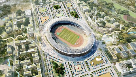 Vogelperspektive auf ein großes, offenes, ovales Stadion mit einer grünen Rasenfläche und einer roten Laufbahn im Zentrum. Das Stadion ist von einem großen Parkplatzgelände im Norden und Westen umgeben, auf dem viele bunte Autos parken. Östlich und südlich erstreckt sich eine parkähnliche Anlage mit Bäumen und modernen, terrassierten Wohngebäuden, die teilweise begrünte Dächer aufweisen.