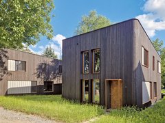 Modernes zweigeschossiges Gebäude mit vertikal verlaufender Holzfassade und großen Fenstern in einer grünen Umgebung