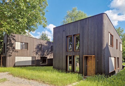 Modernes zweigeschossiges Gebäude mit vertikal verlaufender Holzfassade und großen Fenstern in einer grünen Umgebung