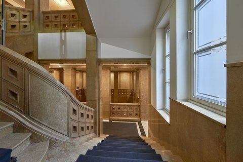 Historisches Treppenhaus mit breiter Steintreppe, Holzgeländer und großen Fenstern mit weißem Rahmen