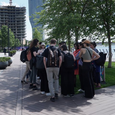 „Eine Gruppe junger Menschen stehen bei sonnigem Wetter entspannt im Kreis, umgeben von einem weitläufigen, urbanen Gebiet.“