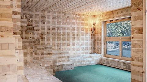 Holzverkleideter Raum mit Sitzstufen, Fenster und grünem Bodenbelag.