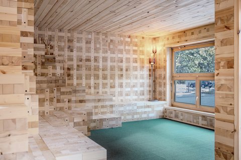 Holzverkleideter Raum mit Sitzstufen, Fenster und grünem Bodenbelag.