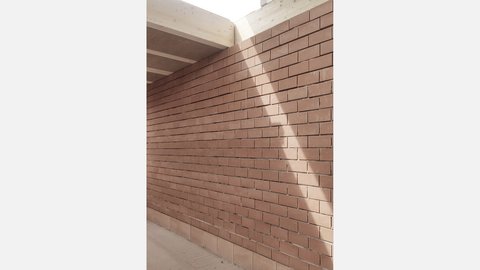 Ziegelwand im Rohbau; ein diagonaler Sonnenstrahl fällt vom Dachfenster über die Oberfläche.