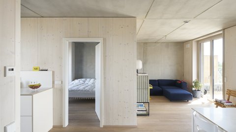 Heller Wohnraum mit Holzoberflächen, Sofa und Zugang zu einem Schlafzimmer.