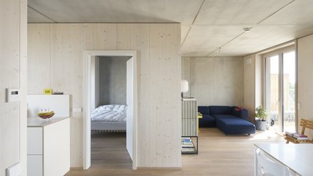 Heller Wohnraum mit Holzoberflächen, Sofa und Zugang zu einem Schlafzimmer.