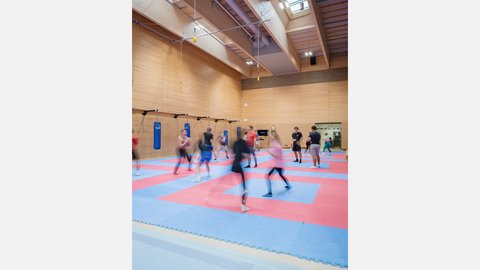Sporthalle mit Trainingsmatten und Sportlerinnen und Sportlern in Bewegung.