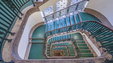 Blick von oben in ein mehrgeschossiges Treppenhaus mit grünem Teppich und grünem Geländer