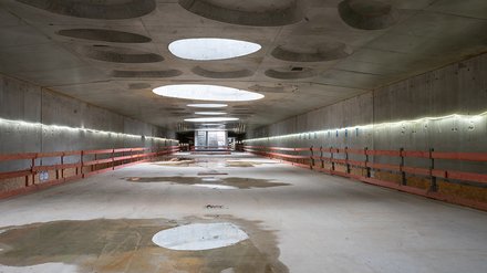 Leerer unterirdischer Tunnel mit Betonwänden und runden Deckenöffnungen.