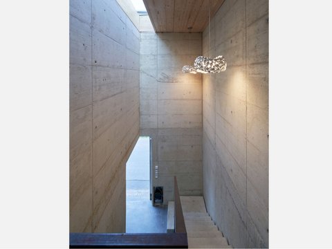 Innenraum mit Sichtbetonwänden, Treppe und modernem Hängeleuchter
