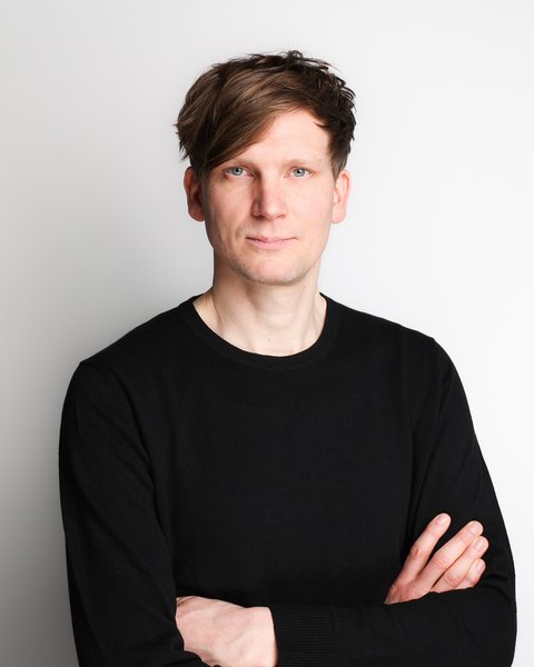 Porträt von Benno Schmitz im schwarzen Pullover mit verschränkten Armen vor hellem Hintergrund.