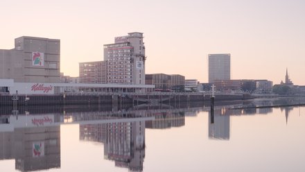 Drei Türme an einem Fluss. Die Gebäude spiegeln sich im Wasser und der Himmel ist rosa und orange