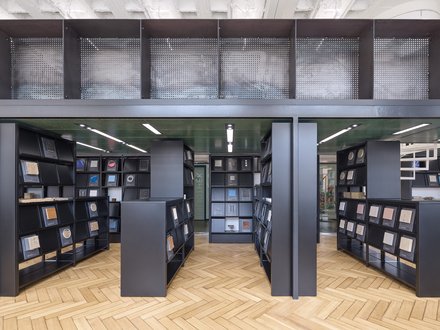 Eine Ansicht eines bibliotheksähnlichen Raums mit schwarzen Regalen, die verschiedene Materialproben halten, wobei natürliches Licht durch große Fenster strömt.