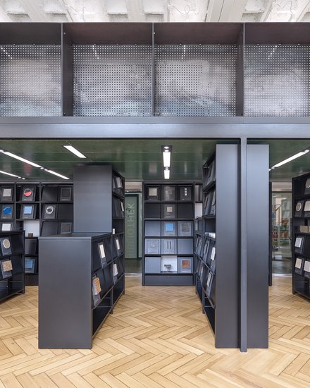 Eine Ansicht eines bibliotheksähnlichen Raums mit schwarzen Regalen, die verschiedene Materialproben halten, wobei natürliches Licht durch große Fenster strömt.