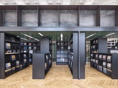 Eine Ansicht eines bibliotheksähnlichen Raums mit schwarzen Regalen, die verschiedene Materialproben halten, wobei natürliches Licht durch große Fenster strömt.