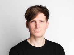 Porträt von Benno Schmitz im schwarzen Pullover mit verschränkten Armen vor hellem Hintergrund.