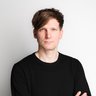 Porträt von Benno Schmitz im schwarzen Pullover mit verschränkten Armen vor hellem Hintergrund.