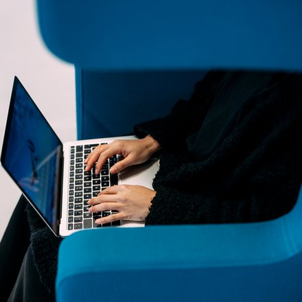 Person sitzt in blauem Sessel und tippt auf Laptop