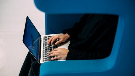 Person sitzt in blauem Sessel und tippt auf Laptop