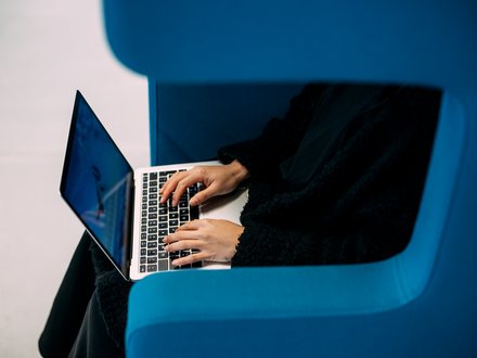 Person sitzt in blauem Sessel und tippt auf Laptop