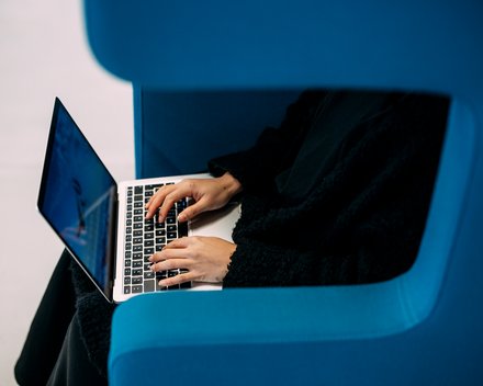 Person sitzt in blauem Sessel und tippt auf Laptop