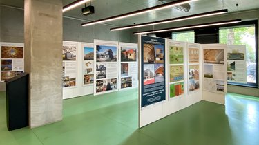 Innenraum einer Ausstellung mit beleuchteten Tafeln zu Holzbauprojekten und Architektur.