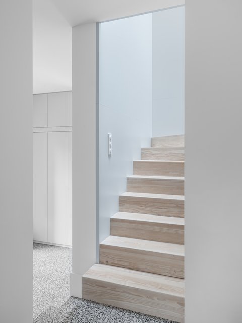 Holztreppe mit hellen Stufen und integrierten Einbauschränken in einem lichtdurchfluteten, minimalistischen Wohnraum.