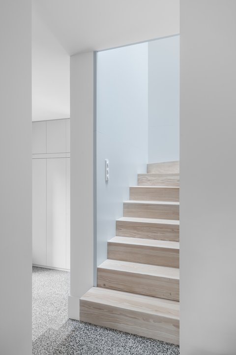 Holztreppe mit hellen Stufen und integrierten Einbauschränken in einem lichtdurchfluteten, minimalistischen Wohnraum.