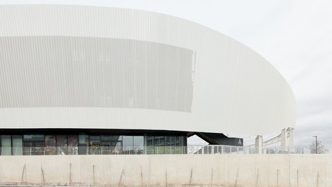 Detailansicht der geschwungenen, weißen Außenfassade des Stadions mit vertikaler Struktur über einer verglasten Erdgeschosszone.