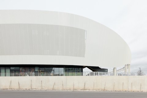 Detailansicht der geschwungenen, weißen Außenfassade des Stadions mit vertikaler Struktur über einer verglasten Erdgeschosszone.