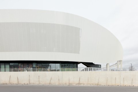 Detailansicht der geschwungenen, weißen Außenfassade des Stadions mit vertikaler Struktur über einer verglasten Erdgeschosszone.