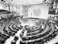 Großer Sitzungssaal mit halbkreisförmigen Sitzreihen und vielen Personen bei einer parlamentarischen Versammlung