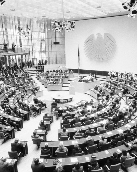 Großer Sitzungssaal mit halbkreisförmigen Sitzreihen und vielen Personen bei einer parlamentarischen Versammlung
