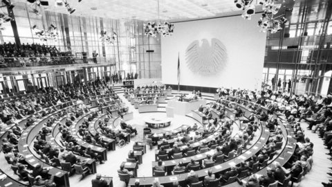 Großer Sitzungssaal mit halbkreisförmigen Sitzreihen und vielen Personen bei einer parlamentarischen Versammlung